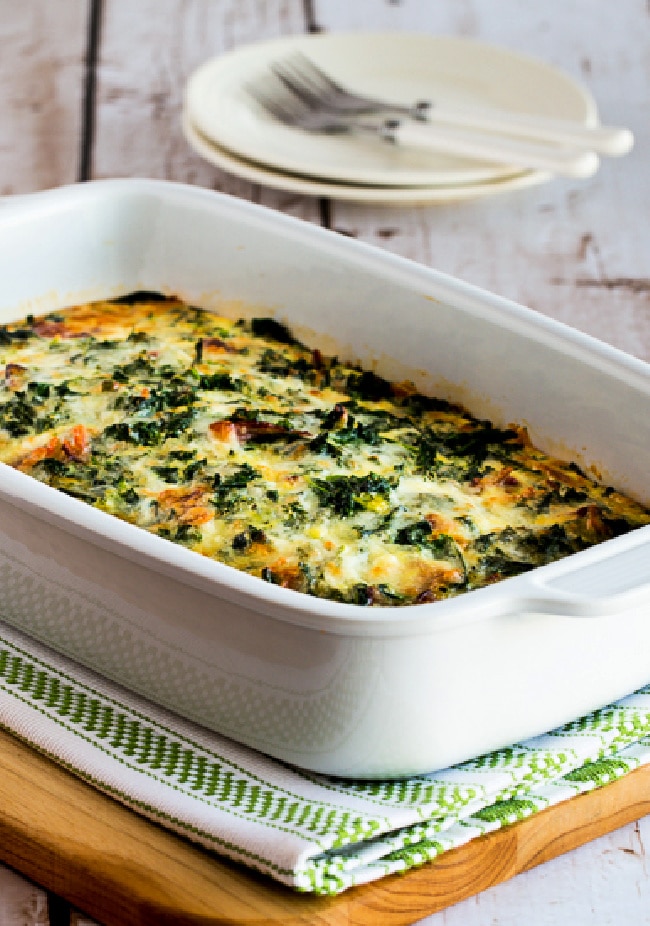 Kale, Bacon, and Cheese Breakfast Casserole shown in baking dish with plates and forks in back.