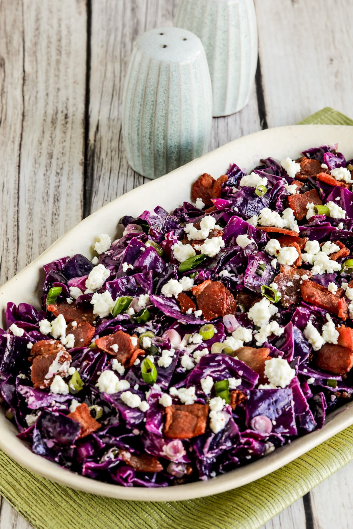 Close-up view of red cabbage salad with bacon and goat cheese on a serving plate with salt and pepper in the background