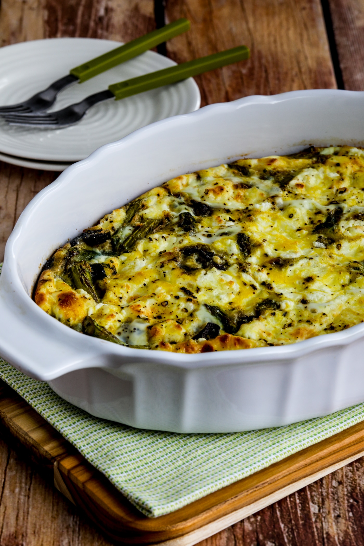 Asparagus, Mushroom, and Goat Cheese Breakfast Casserole in baking dish shown on napkin with plates, forks