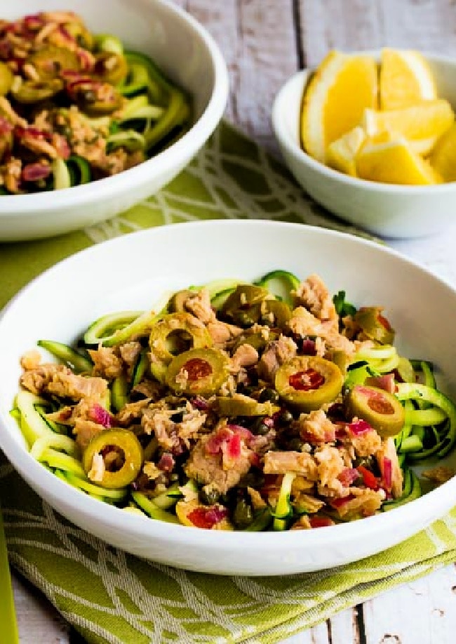 Cropped image of Zucchini Noodles with Tuna and Green Olives in two serving bowls, with lemons.