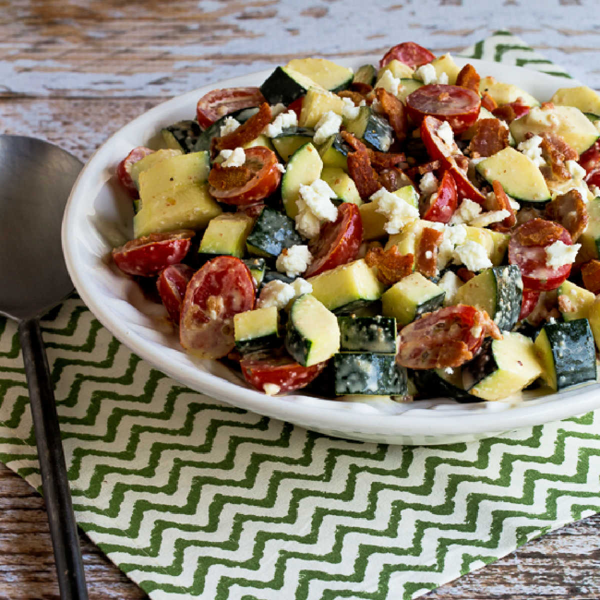 Raw Zucchini Salad with Bacon, Tomato, and Feta shown in serving bowl on napkin.