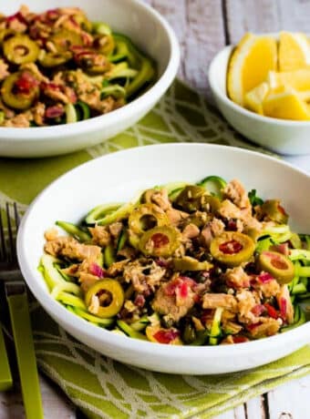 Square image of Tuna Zucchini Noodles with Green Olives shown in two serving bowls with lemons on the side.