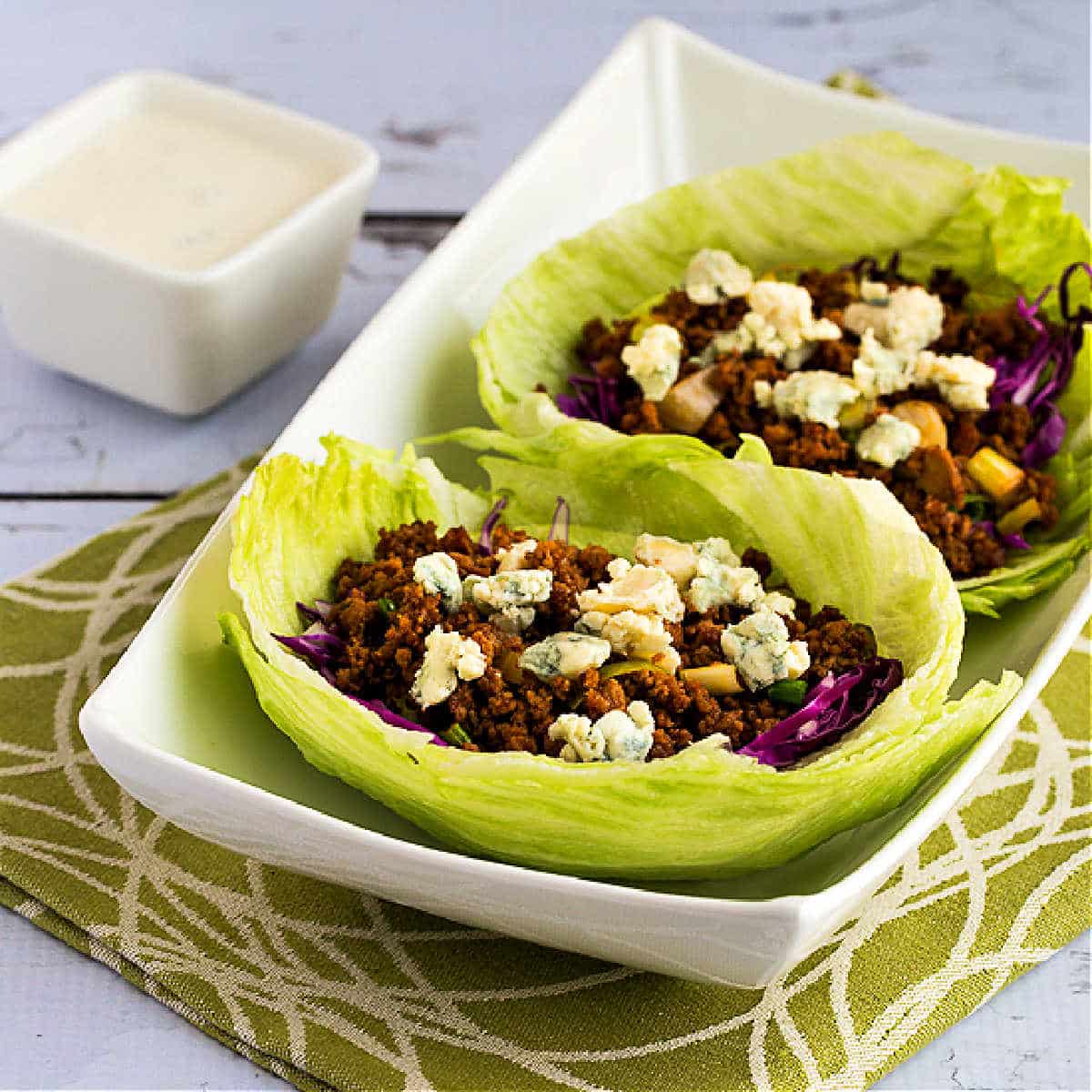 Square image of Buffalo Chicken or Turkey Lettuce Wraps in serving dish on green-white-napkin.