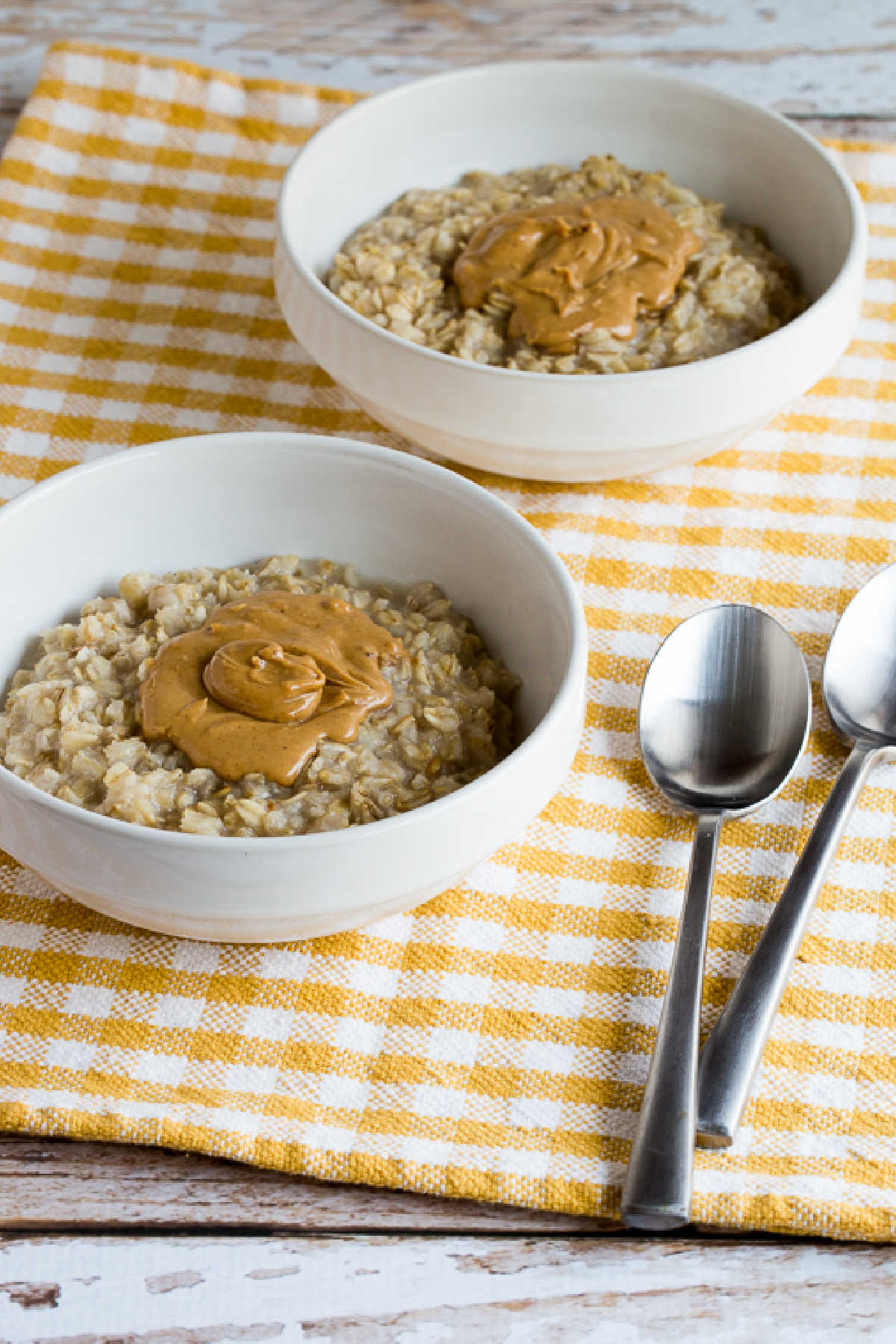 Peanut Butter Oatmeal in two serving bowls with yellow-white checked napkin and spoons