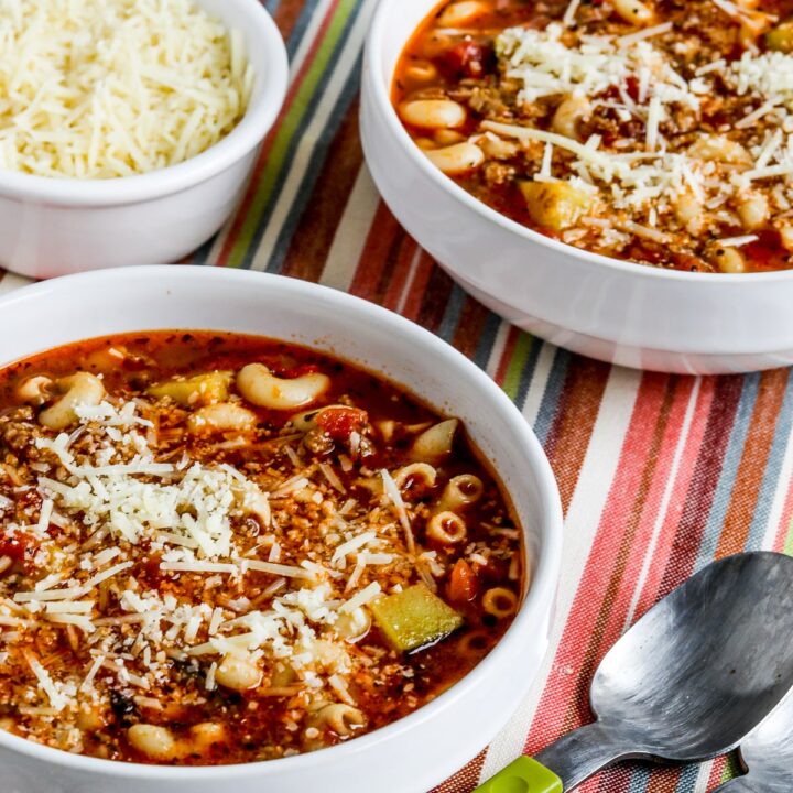 Italian Sausage, Zucchini, and Macaroni Soup shown in two bowls with spoons and Parmesan