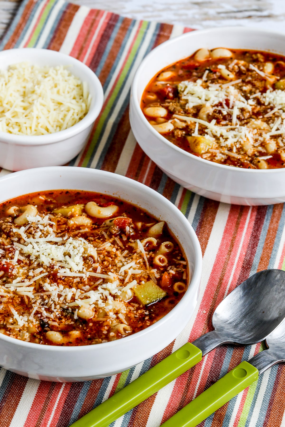Italian Sausage, Zucchini, and Macaroni Soup shown in two bowls with spoons and Parmesan