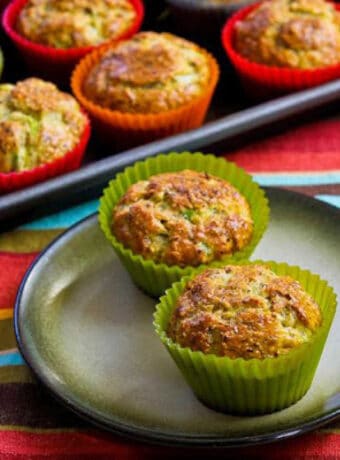 square image of Savory Breakfast Muffins with two muffins on plate and baking sheet of muffins in background