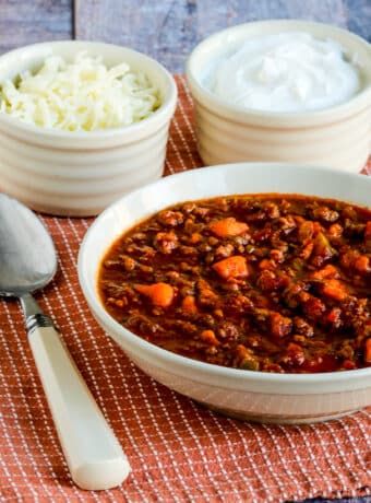 Square image for Turkey Sweet Potato Chili with bowl of chili, spoon, sour cream, and cheese on napkin.