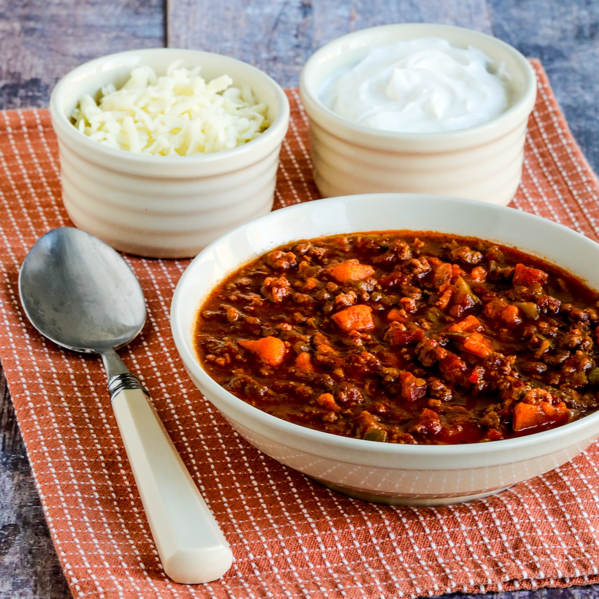 Square image for Turkey Sweet Potato Chili with bowl of chili, spoon, sour cream, and cheese on napkin.