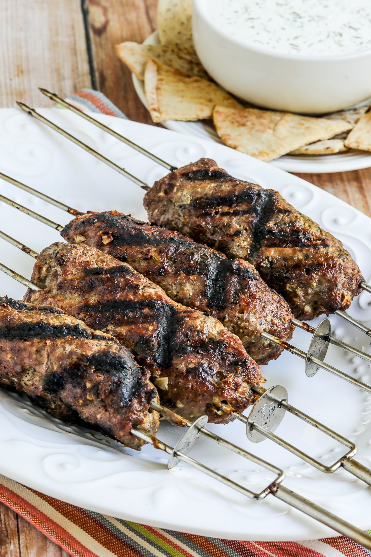 Kabob Koobideh shown on serving plate with Tzatziki in back.