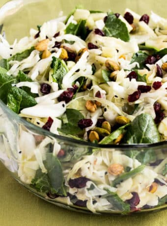 Square image of Cabbage Apple Salad shown in glass bowl on green napkin.