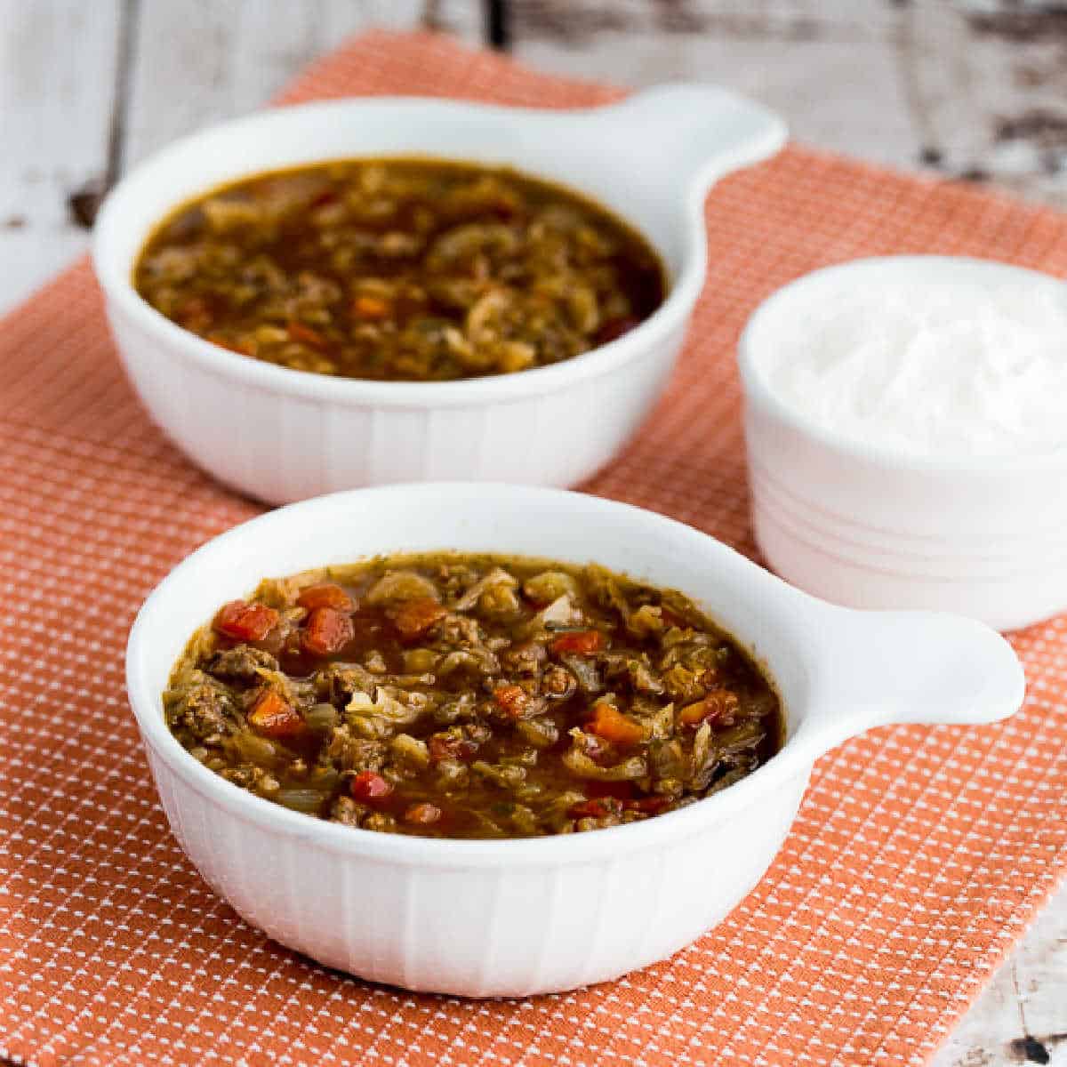 Ground Beef and Sauerkraut Soup shown in two serving bowls with sour cream on the side