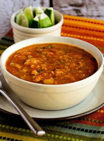Square image of Mexican Red Lentil Stew in serving bowl on napkin, with limes in background.
