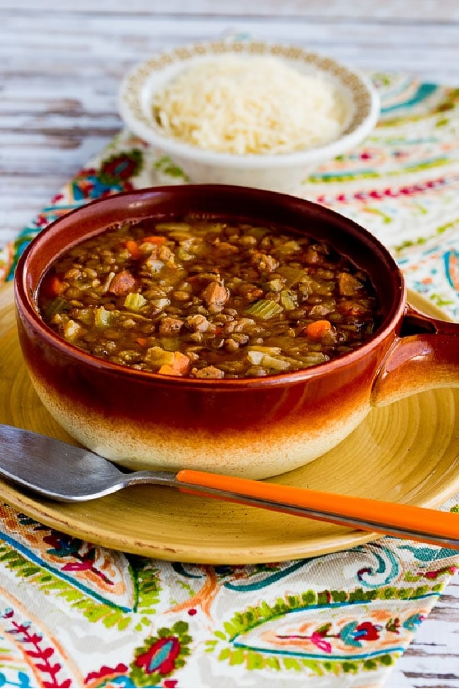 Lentil, Sausage, and Cabbage Soup in serving bowl with Parmesan cheese on side