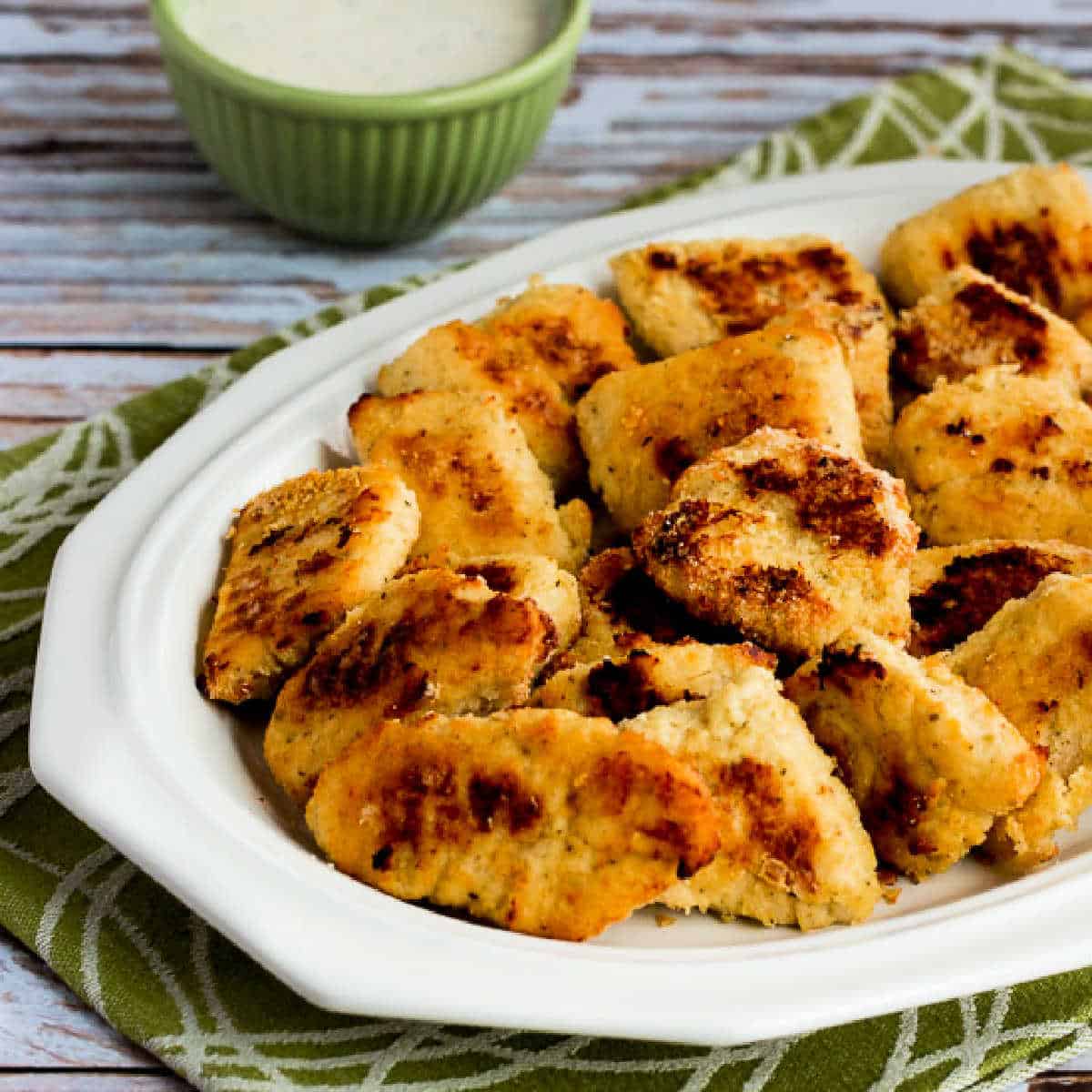 Baked Chicken Nuggets on serving plate with Ranch dipping sauce in background.