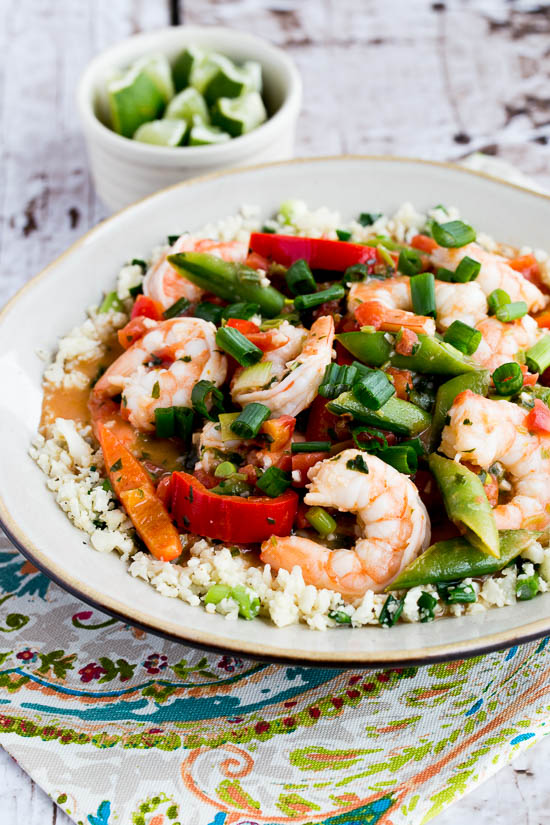 Coconut Milk Shrimp in serving bowl over cauliflower rice with limes in background