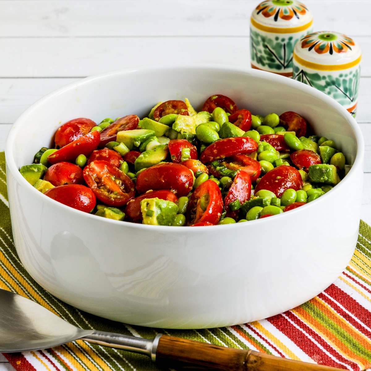 Square photo of tomato and avocado salad with edamame, shown in serving bowl.