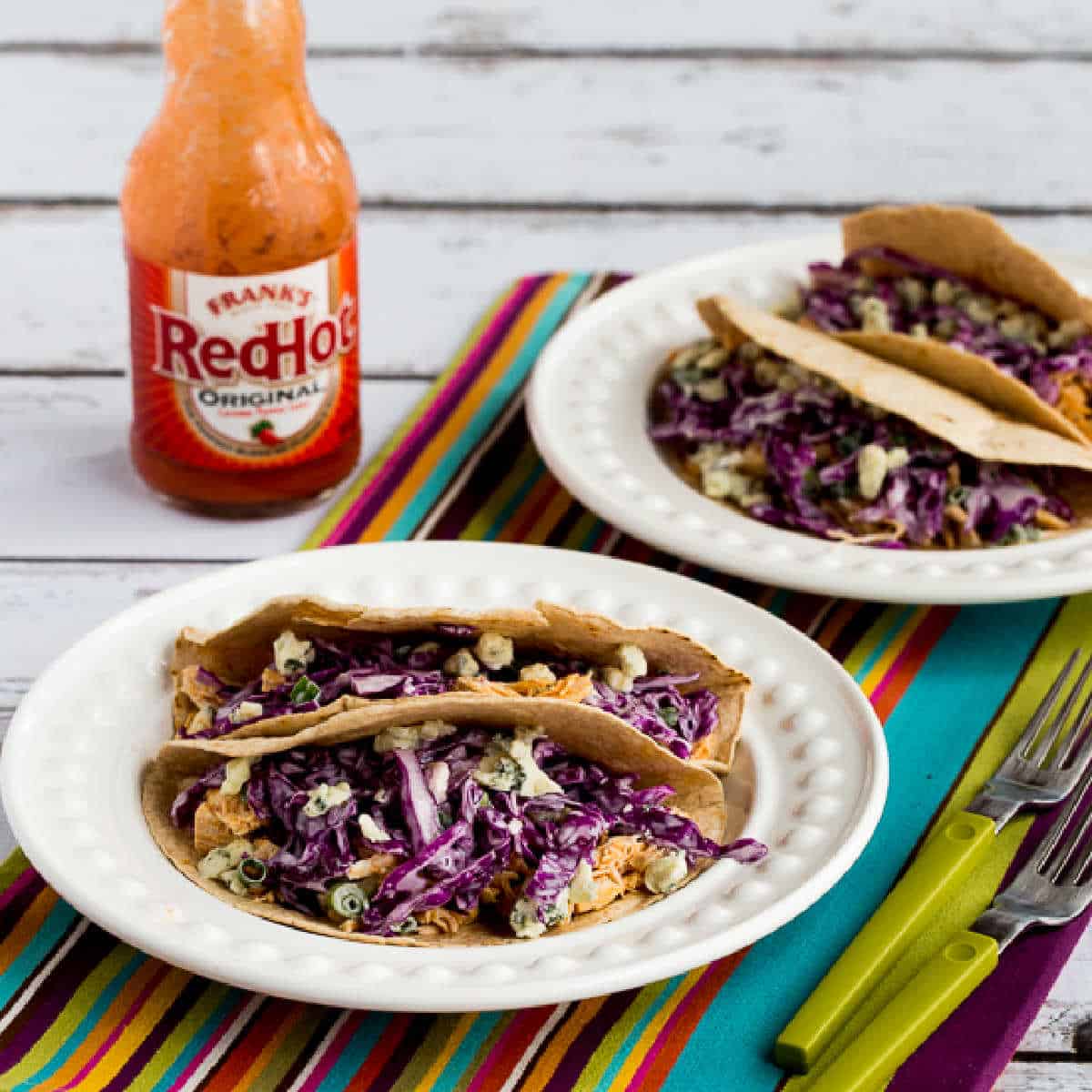 Buffalo Chicken Tacos shown on serving plate with vibrant striped napkin, forks, and Red Hot Sauce.