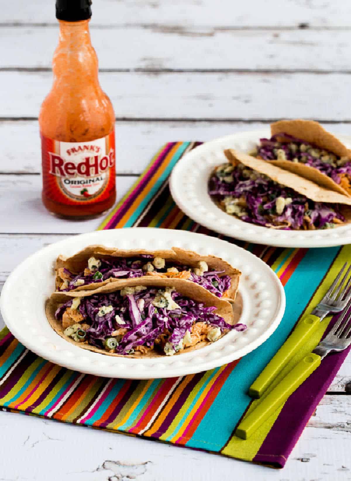 buffalo chicken tacos on two serving plates with Frank's Red Hot Sauce in background