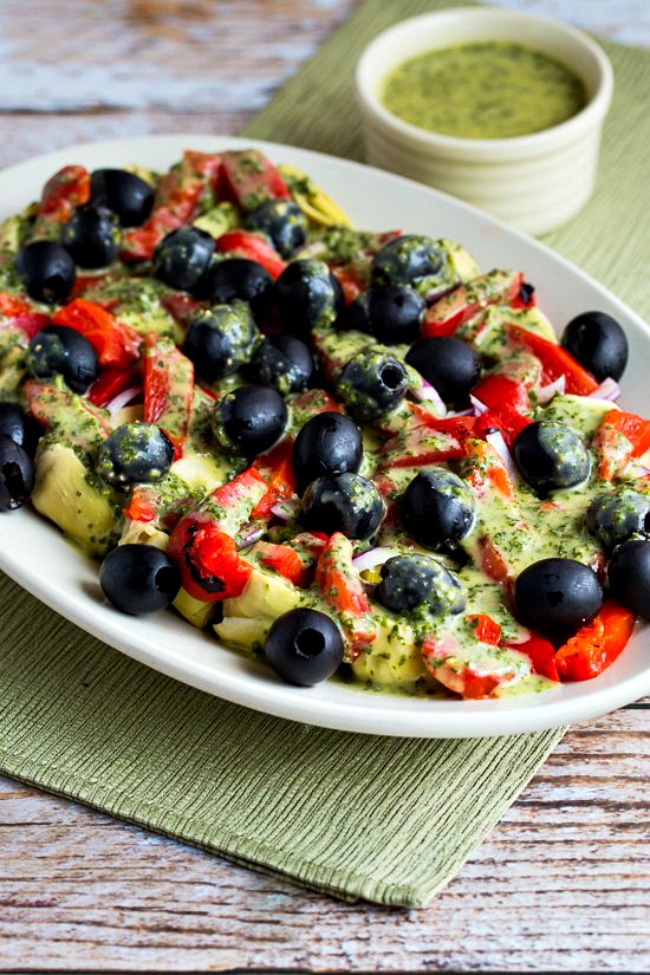 Photo of Antipasto Artichoke Salad on serving platter with green napkin and basil vinaigrette.