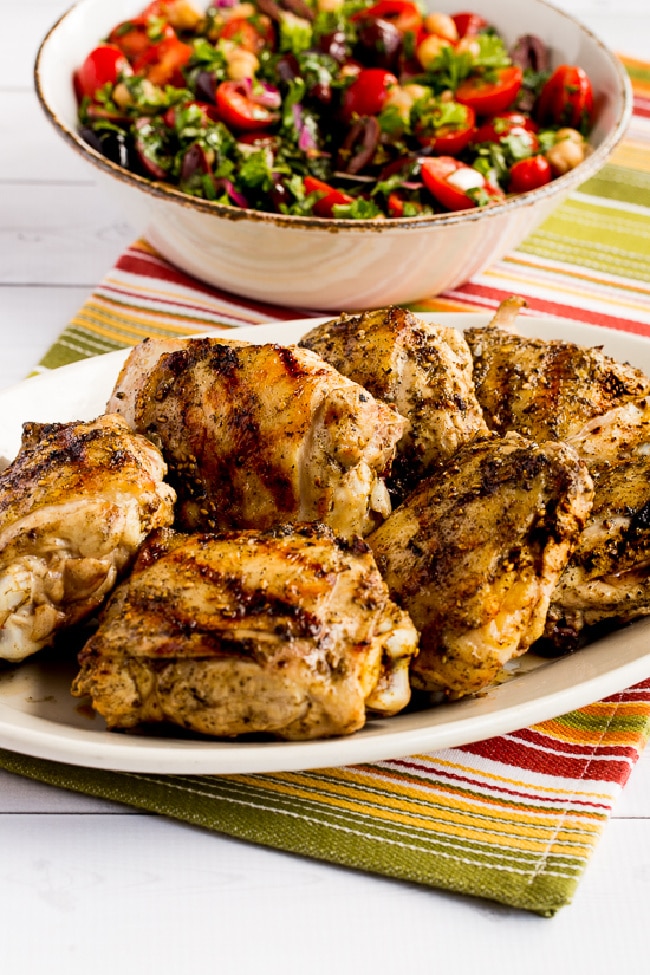 Grilled Chicken Thighs with Lemon and Za'atar shown on serving plate with salad in background