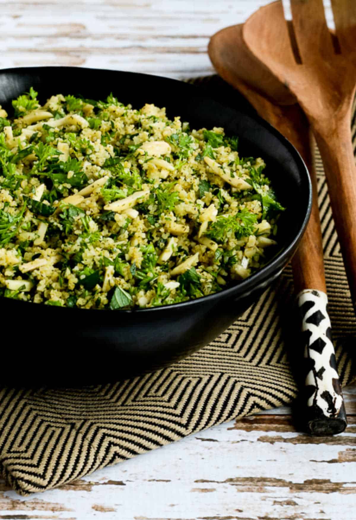 Tabbouleh Salad with Almonds in serving bowl with black/gold napkin and serving forks