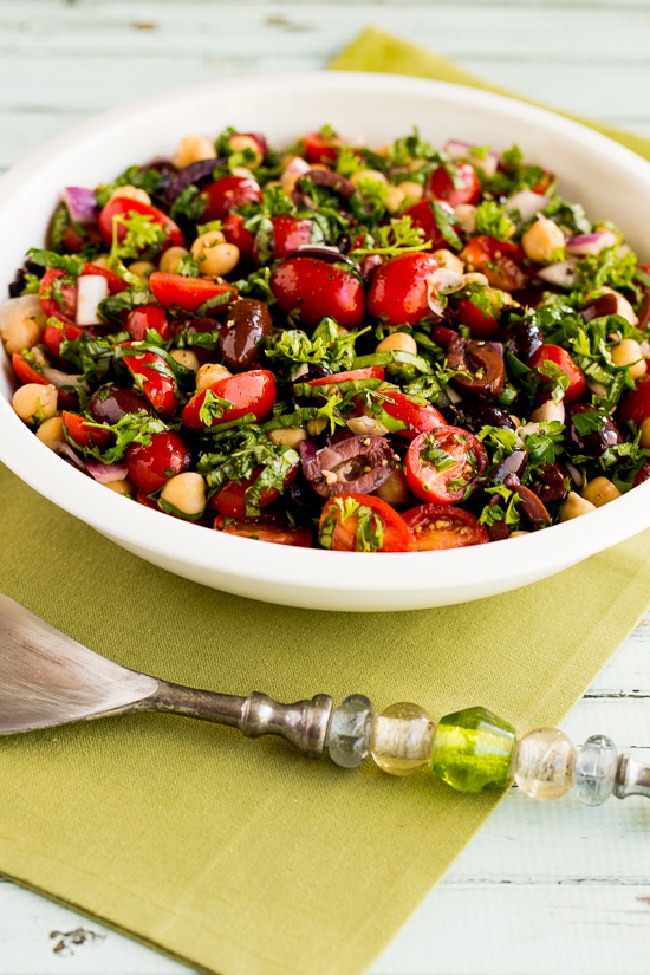 Chickpea Salad with Tomatoes, Olives, and Herbs in serving bowl with fork and green napkin