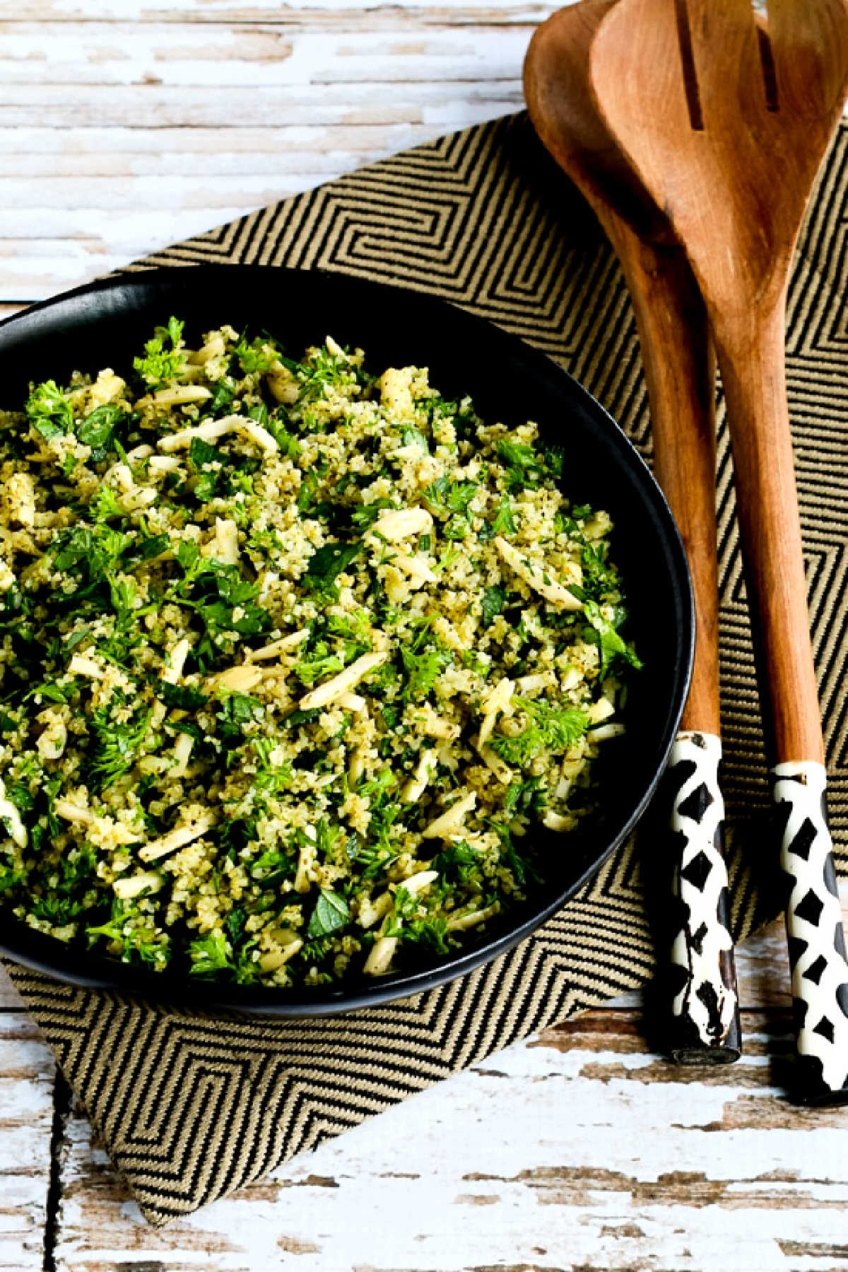 Tabbouleh Salad with Almonds shown in serving bowl with colorful black and white serving forks