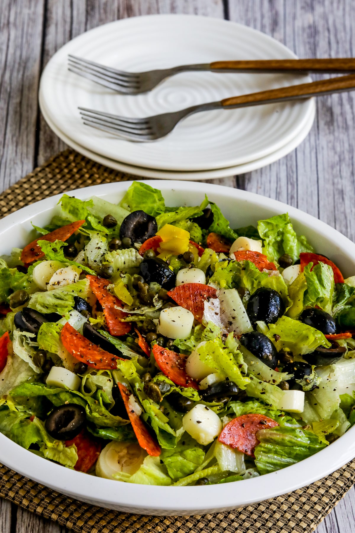 Chopped Antipasto Salad shown in serving bowl with plates and forks in back.