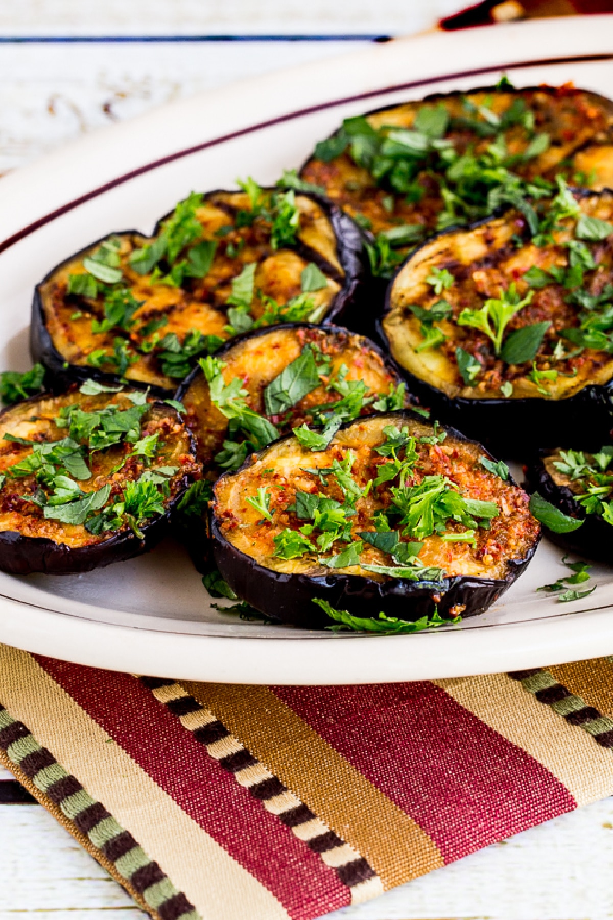 Spicy Grilled Eggplant shown on serving plate with fresh herbs and colorful napkin