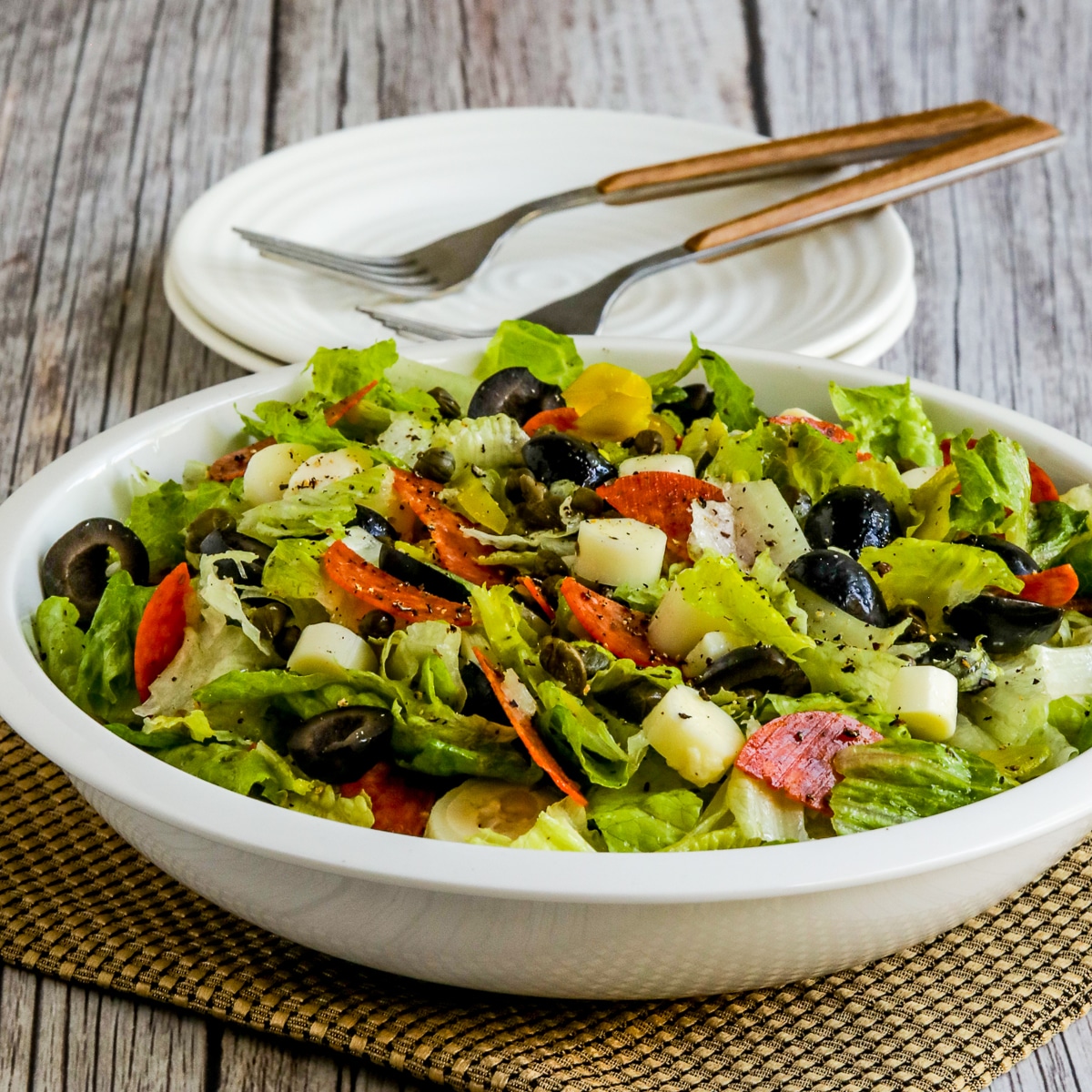 Square image for Chopped Antipasto Salad shown in serving bowl with plates and forks.