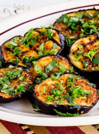 square image of Spicy Grilled Eggplant shown on serving plate with fresh herbs sprinkled over