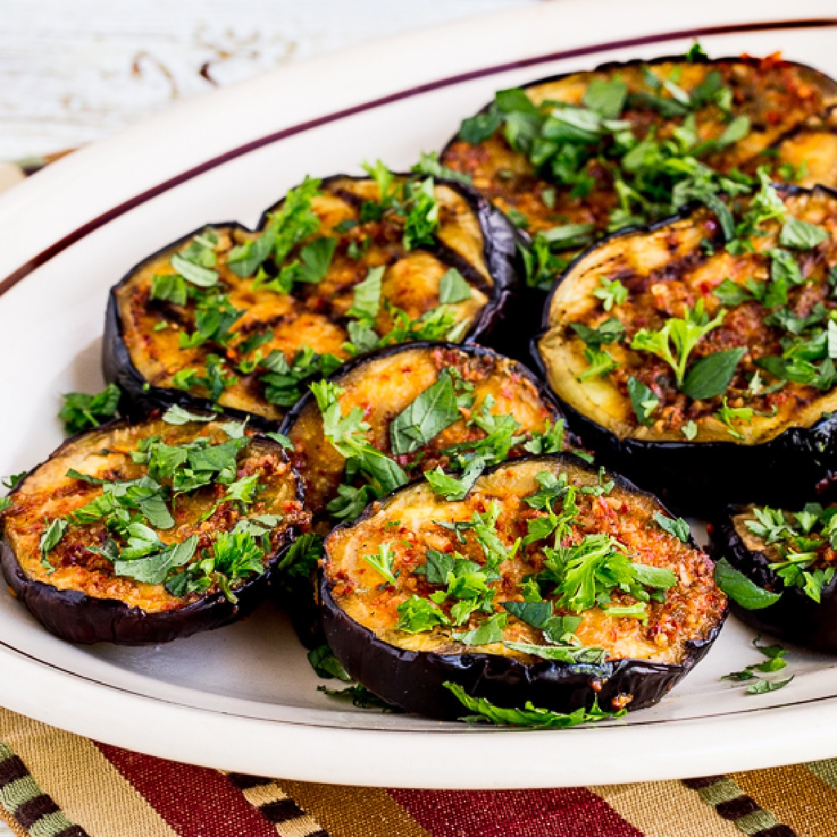 square image of Spicy Grilled Eggplant shown on serving plate with fresh herbs sprinkled over