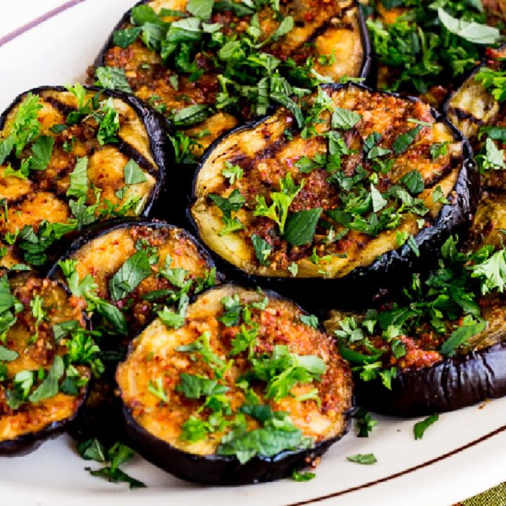 Spicy Grilled Eggplant shown on serving plate with fresh herbs sprinkled over
