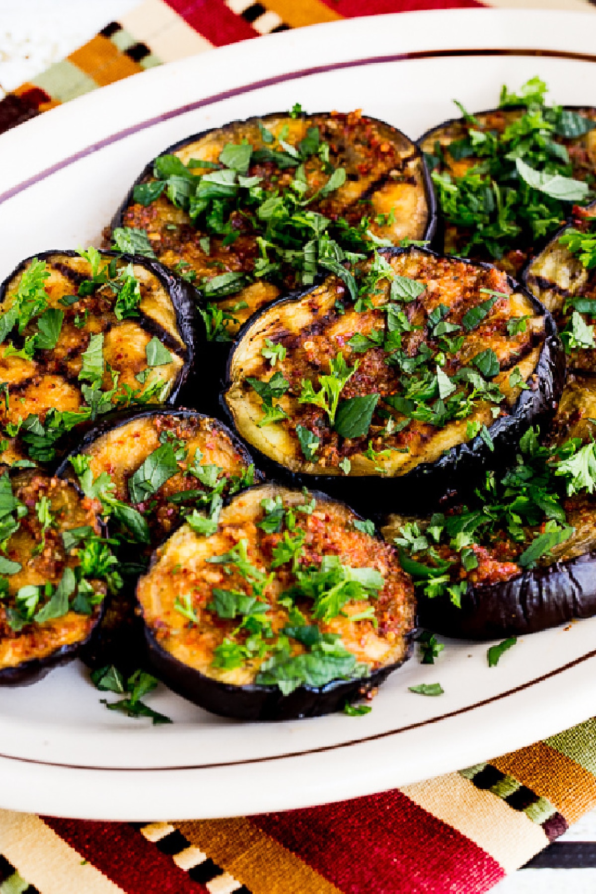 Spicy Grilled Eggplant shown on serving plate with fresh herbs sprinkled over