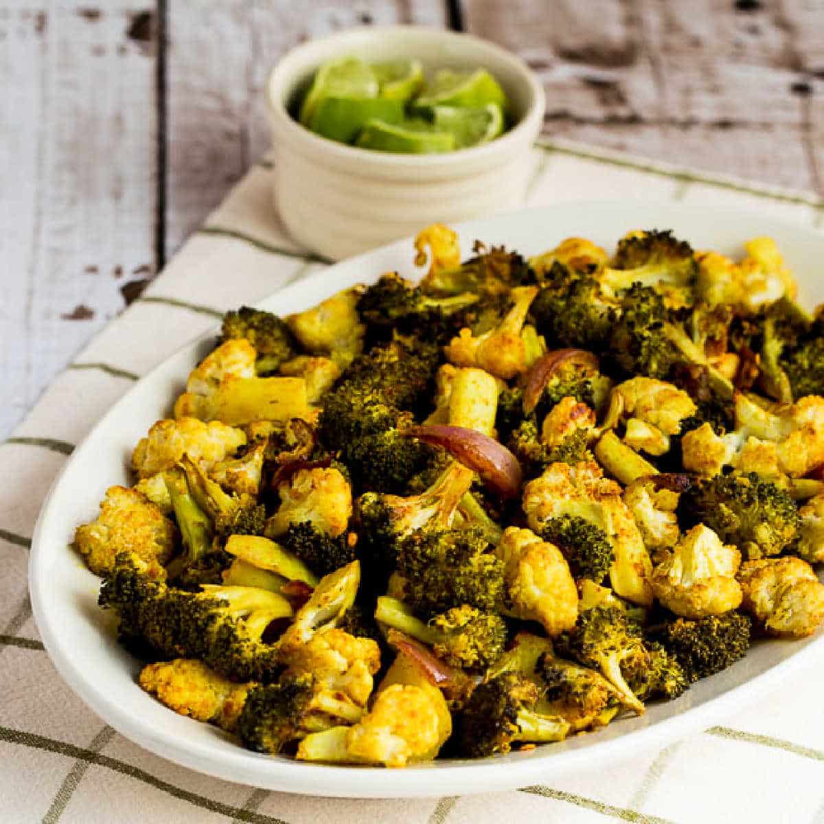 square image of Roasted Broccoli and Cauliflower shown on serving plate with limes in background
