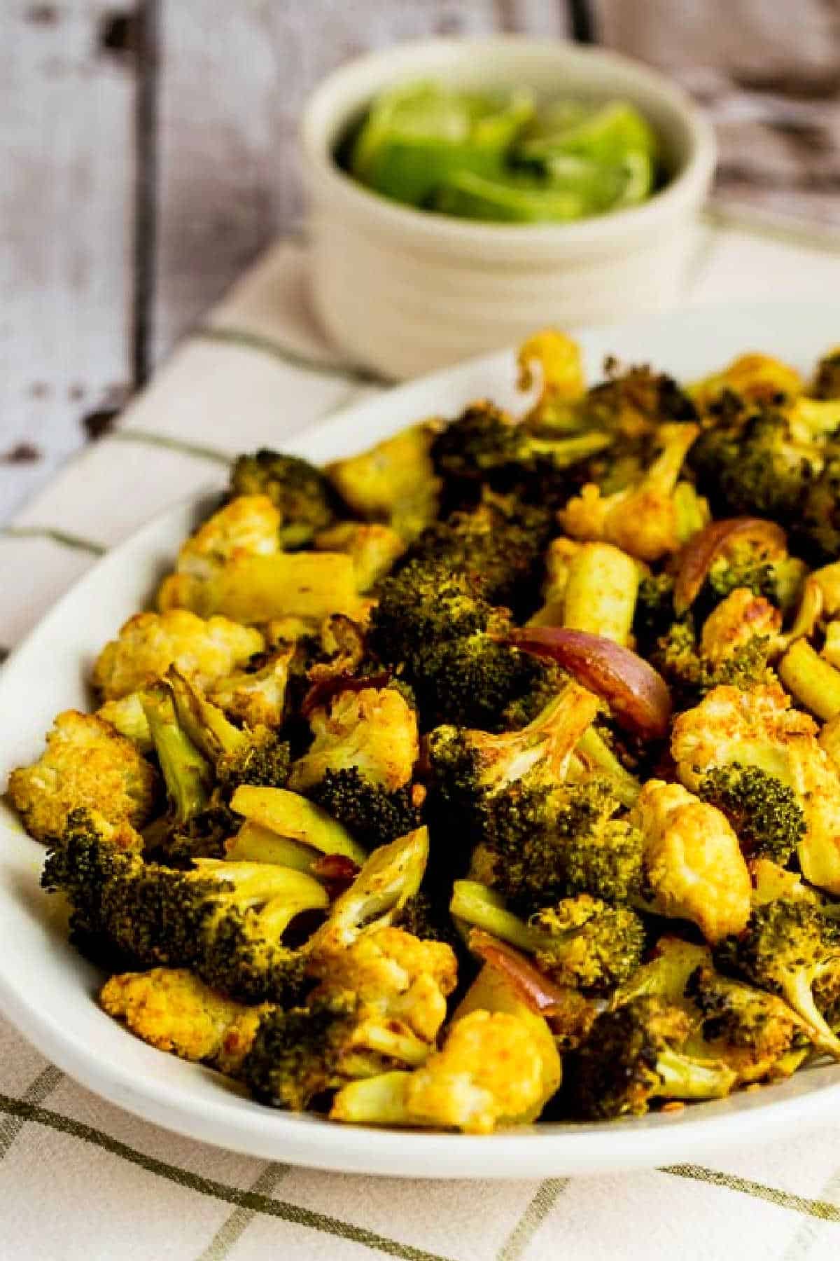 Roasted Broccoli and Cauliflower shown on serving plate with limes in background