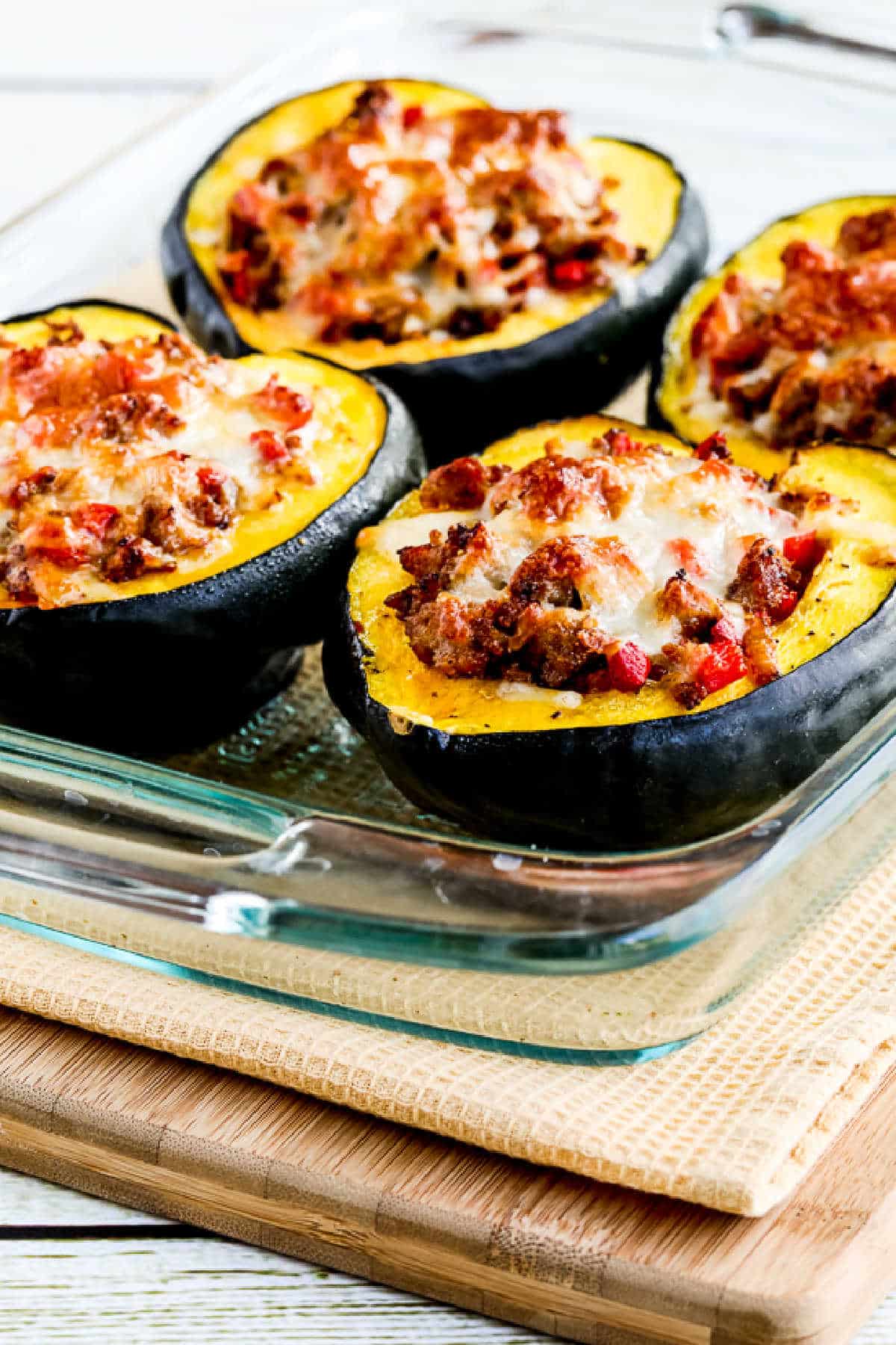 Sausage stuffed with acorn squash in a baking dish on a cutting board