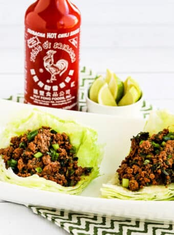 Sriracha Beef Lettuce Wraps shown on serving plate with Sriracha in back.