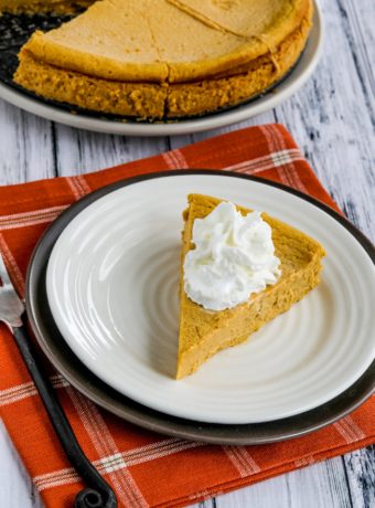 Sugar-Free Pumpkin Cheesecake Pie shown on serving plate with rest of pie on plate in background