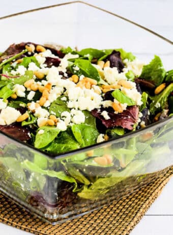 Square image of Spring Mix Salad in glass serving bowl with pine nuts and Feta.