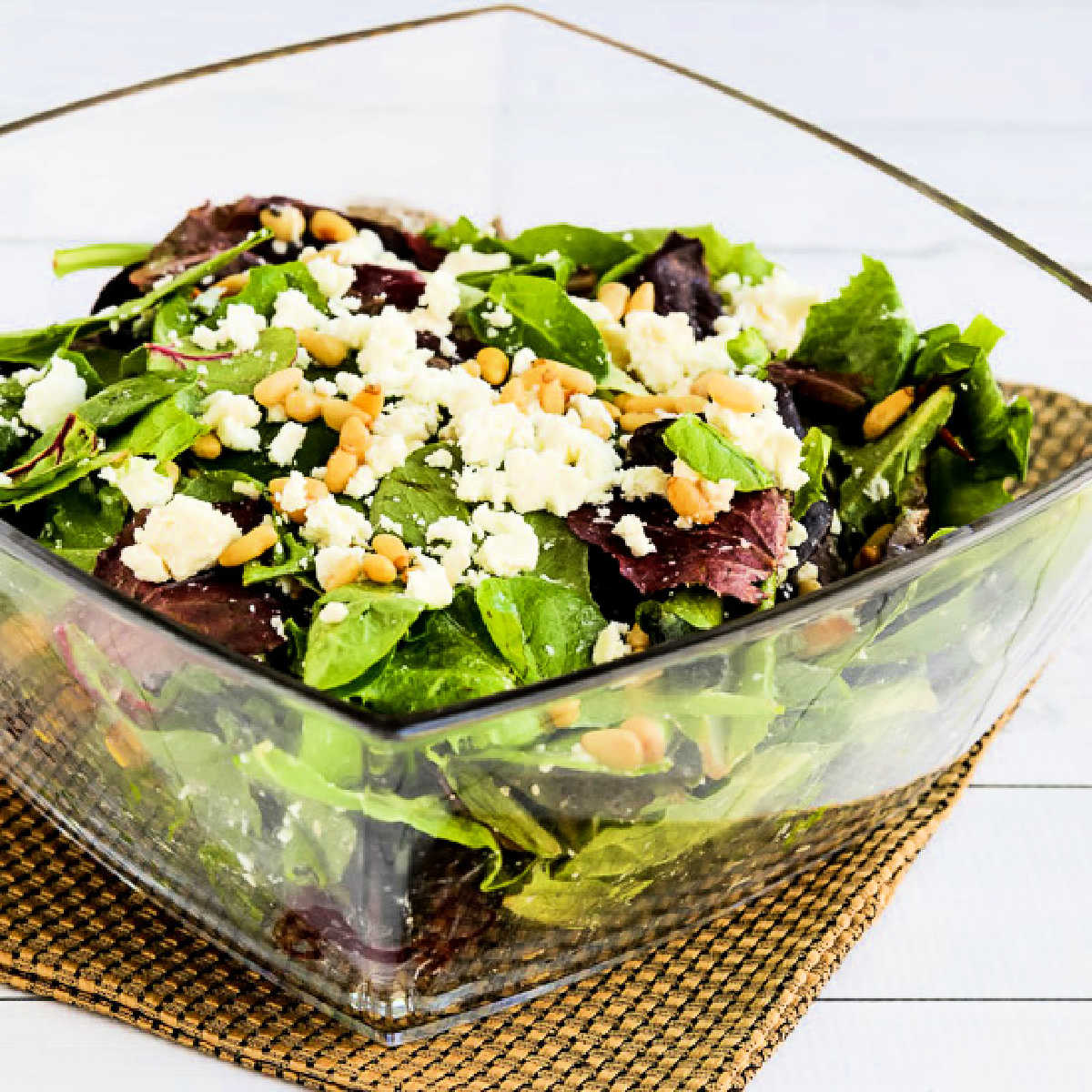 Square image of Spring Mix Salad in glass serving bowl with pine nuts and Feta.