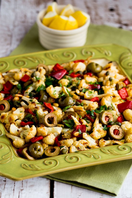 Roasted Cauliflower with Red Peppers, Green Olives, and Pine Nuts shown on green serving plate.