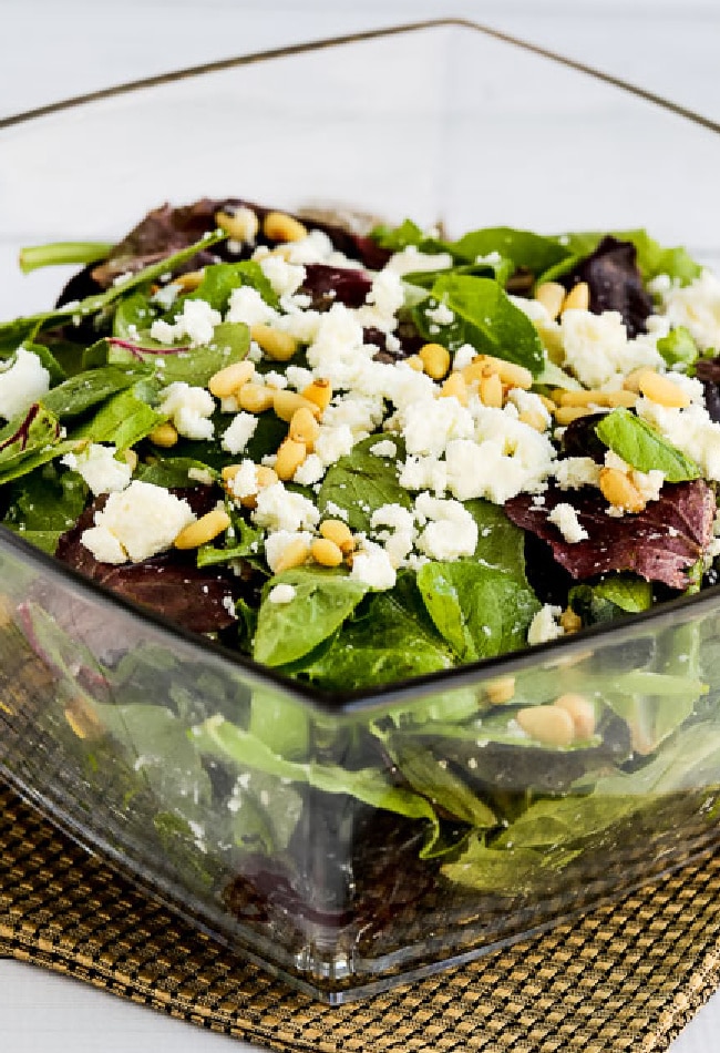 Cropped image of Spring Mix Salad shown in glass bowl with Feta and pine nuts.