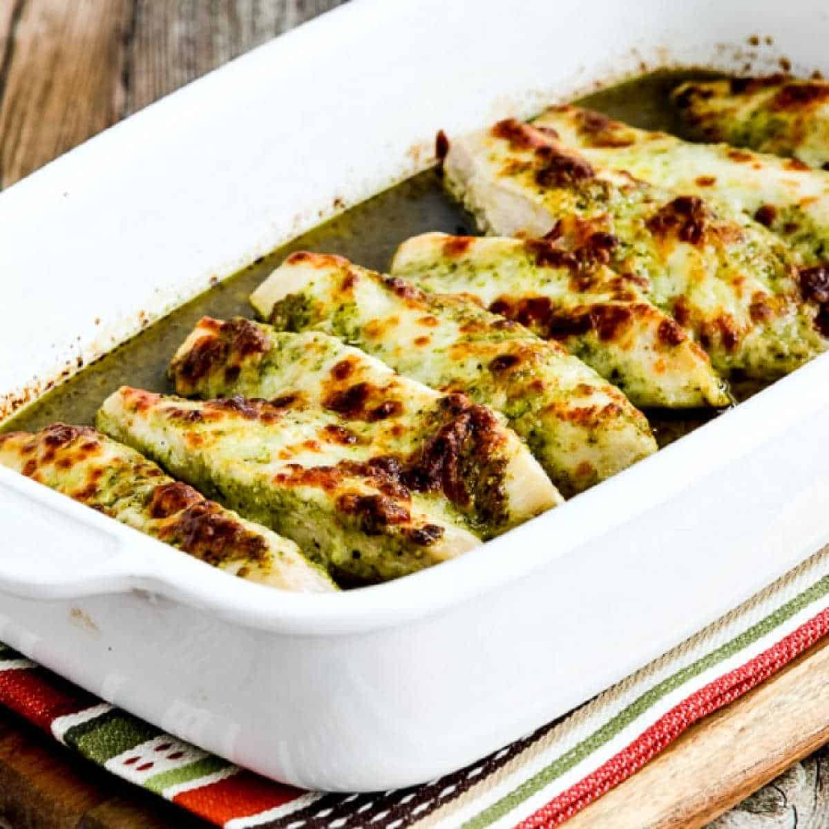 Square image of pesto chicken baked in a baking dish on a striped napkin