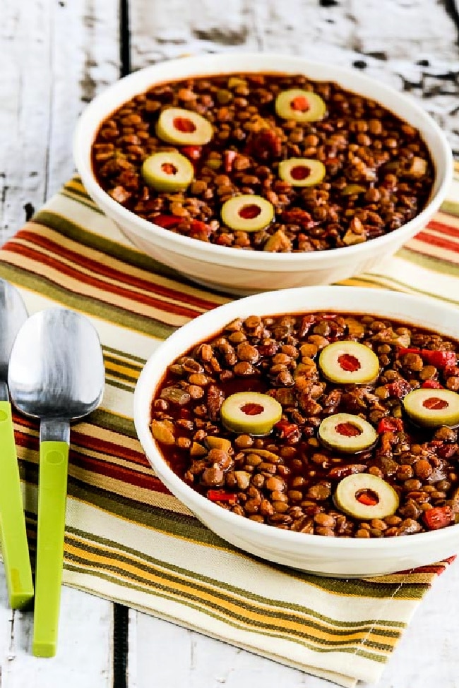  Vegan Picadillo (with Lentils, Peppers, and Green Olives) shown in two serving bowls with spoons and striped napkin.