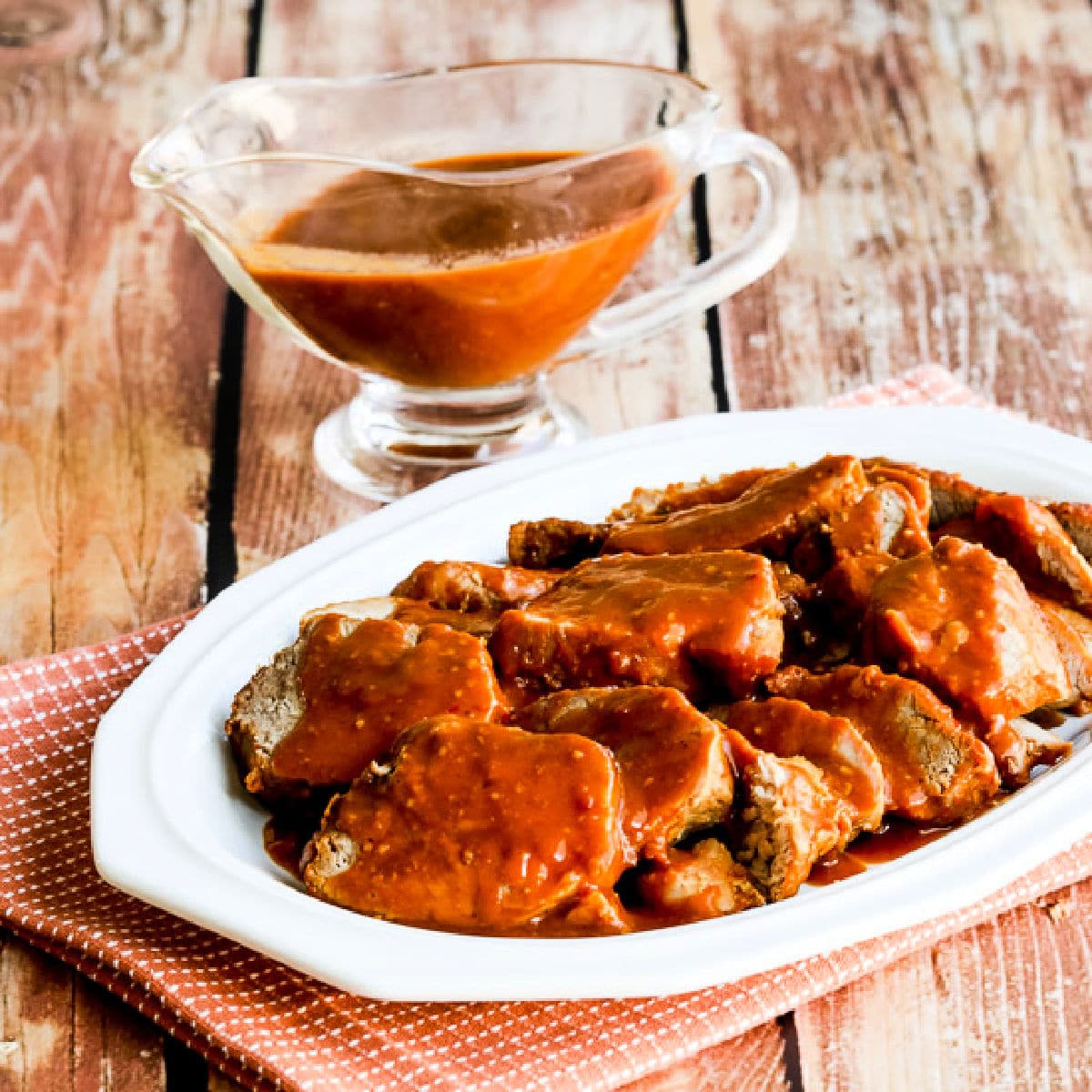 Square image of Slow Cooker Pork with Peanut Sauce shown on serving platter with sauce in background.