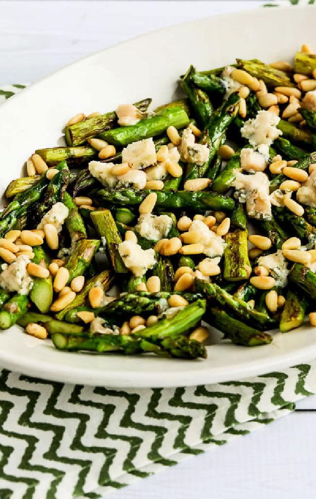 Pan-fried asparagus with gorgonzola and pine nuts shown on green-white napkin serving plate.