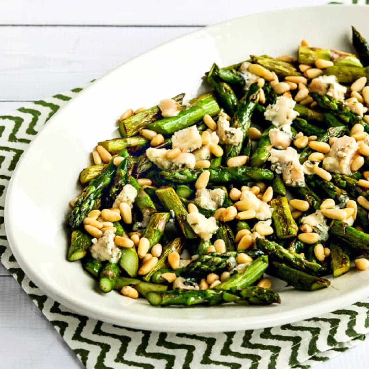 Pan-Fried Asparagus with Gorgonzola and Pine Nuts shown on serving plate on green and white napkin.