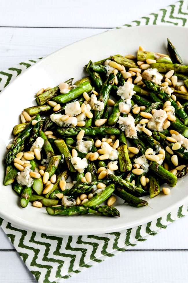 A closeup photo of a frying pan of asparagus with gorgonzola and pine nuts